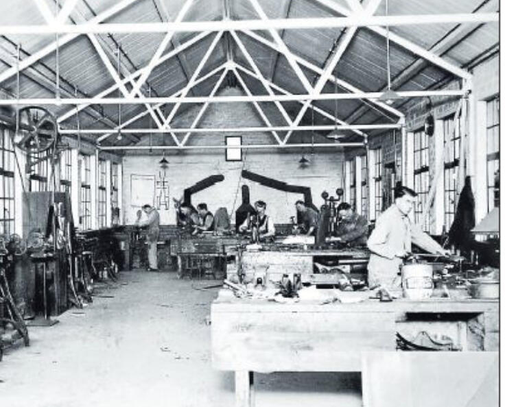 Untitled Black and white archive photo of a workshop with high steel-trussed ceilings, showing several workers at benches and machinery, connected to Emily Kathleen Renshaw's history.